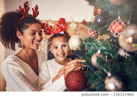 Christmas, portrait and mother with girl decorating tree, bonding and happy together. Xmas, smile and face of kid with African mom with ornament for family party, celebration or holiday event in home Christmas, portrait and mother with girl decorating tree, bonding and happy together. Xmas, smile and face of kid with African mom with ornament for family party, celebration or holiday event in home 136313468