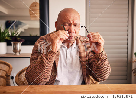 Glasses, vision and a senior man at a table in the living room of his home during retirement. Thinking, relax and eyesight with an elderly male person holding prescription frame lenses in his house Glasses, vision and a senior man at a table in the living room of his home during retirement. Thinking, relax and eyesight with an elderly male person holding prescription frame lenses in his house 136313971