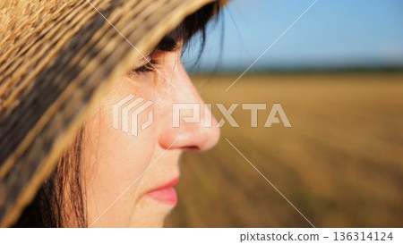 Female farmer in straw hat looking into wheat field and examining plantation at sunset. Close up face of adult beautiful woman illuminating by bright rays of sun. Concept of agriculture business Female farmer in straw hat looking into wheat field and examining plantation at sunset. Close up face of adult beautiful woman illuminating by bright rays of sun. Concept of agriculture business 136314124