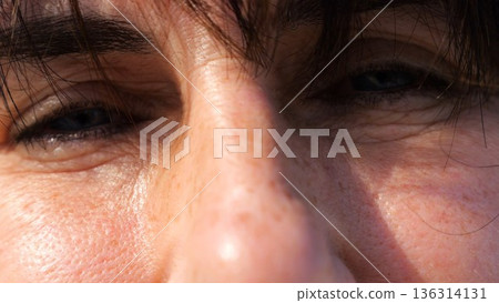 Tired blue eyes of a female blinking and looking into camera outdoor. Face of adult woman illuminating by bright rays of sun. Upset facial expression of lady. Close up Slow motion Tired blue eyes of a female blinking and looking into camera outdoor. Face of adult woman illuminating by bright rays of sun. Upset facial expression of lady. Close up Slow motion 136314131