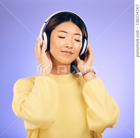 Headphones, music and happy Asian woman relax in studio for streaming app, subscription and radio. Calm, podcast and isolated female person listening to audio, song and track on purple background 136314167