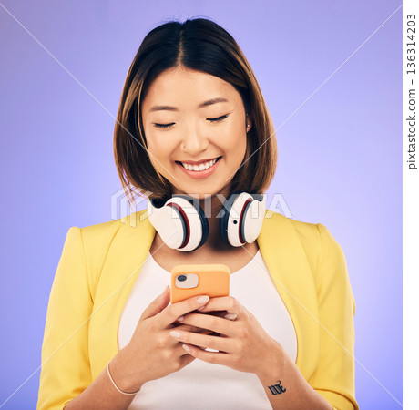 Social media, phone and happy Asian woman in studio for text message, internet meme and chat. Headphones, smile and female person on smartphone listen to audio, song and track on purple background Social media, phone and happy Asian woman in studio for text message, internet meme and chat. Headphones, smile and female person on smartphone listen to audio, song and track on purple background 136314203