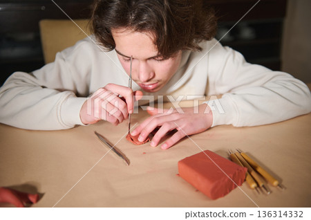 Young Boy Molding Clay at Home, Focused on Sculpting with Tools and Red Clay Block Young Boy Molding Clay at Home, Focused on Sculpting with Tools and Red Clay Block 136314332