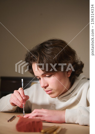 Teen Boy Molding Clay at Home: Focused Hobbyist Creating Small Sculptures Teen Boy Molding Clay at Home: Focused Hobbyist Creating Small Sculptures 136314334