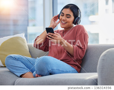 Relax, music and phone with woman on sofa and dance for streaming, social media and audio. Happy, technology and radio with person listening to headphones in living room at home for energy and sound 136314356