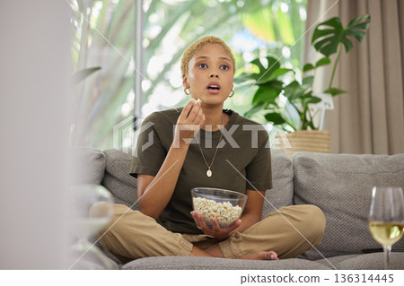 Surprise, watching tv and a woman on the sofa with popcorn for a movie or show. Wow, house and a young girl eating a snack while on the living room couch for a horror, film or streaming a drama Surprise, watching tv and a woman on the sofa with popcorn for a movie or show. Wow, house and a young girl eating a snack while on the living room couch for a horror, film or streaming a drama 136314445