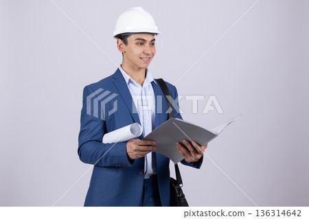 Young man in blue suit and white hardhat holding a plan 136314642