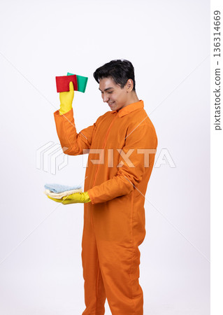 Young man in orange uniform holding paint rollers and brushes Young man in orange uniform holding paint rollers and brushes 136314669