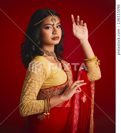 Portrait, beauty and Indian woman with fashion, traditional dress and luxury against a red studio background. Face, female person and model with cultural clothes, jewellery and gold with religion Portrait, beauty and Indian woman with fashion, traditional dress and luxury against a red studio background. Face, female person and model with cultural clothes, jewellery and gold with religion 136315096
