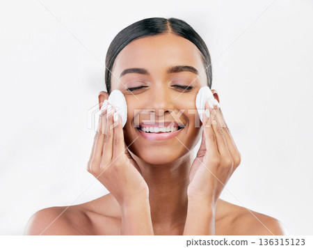 Woman, smile and cotton pad for face, cosmetics and aesthetic skincare in studio on white background. Happy indian female model with beauty products for cleaning, facial dermatology or makeup removal Woman, smile and cotton pad for face, cosmetics and aesthetic skincare in studio on white background. Happy indian female model with beauty products for cleaning, facial dermatology or makeup removal 136315123