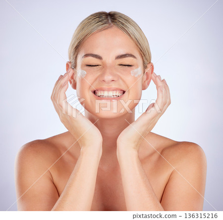 Beauty, face and happy woman with cream application for facial hydration, dermatology or glowing skincare. Studio, lotion or person smile for success of acne prevention product on grey background Beauty, face and happy woman with cream application for facial hydration, dermatology or glowing skincare. Studio, lotion or person smile for success of acne prevention product on grey background 136315216