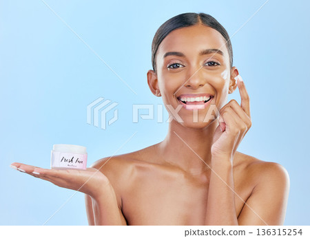 Face cream, skin and beauty portrait of a happy woman with natural glow on a blue background. Dermatology, moisturizer and cosmetics of Indian female model with a product container on hand in studio 136315254