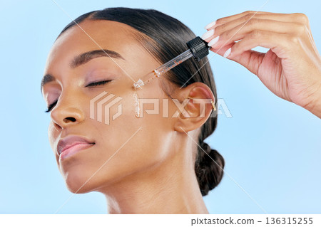Beauty, face serum and a woman with skin care on a blue background with a cosmetics dropper. Dermatology, natural glow and Indian female model for facial shine, wellness and self love in studio 136315255
