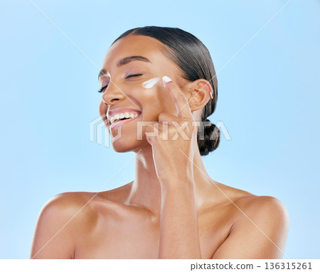 Face cream, skin and beauty of a happy woman with natural glow on a blue background. Dermatology, moisturizer and cosmetics of an Indian female model for facial shine, wellness or self care in studio 136315261