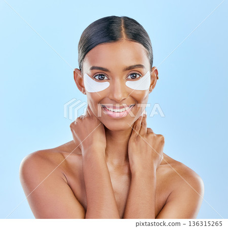 Eye patch, portrait and beauty of a woman with natural skin glow on a blue background. Dermatology, collagen face mask and cosmetics of Indian female model for facial shine and self care in studio Eye patch, portrait and beauty of a woman with natural skin glow on a blue background. Dermatology, collagen face mask and cosmetics of Indian female model for facial shine and self care in studio 136315265
