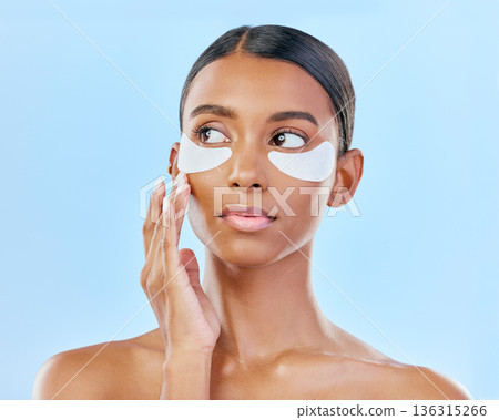 Face, eye patch and beauty of a woman with natural skin glow on a blue background. Dermatology, collagen mask and cosmetics of Indian female model for facial shine, wellness or self care in studio Face, eye patch and beauty of a woman with natural skin glow on a blue background. Dermatology, collagen mask and cosmetics of Indian female model for facial shine, wellness or self care in studio 136315266