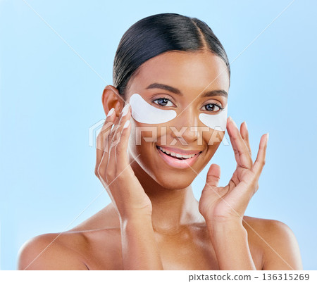 Happy, skincare and portrait of woman with patches for eyes, dark circles and treatment. Smile, face and Indian girl or model with a facial collagen for a glow isolated on a blue background in studio Happy, skincare and portrait of woman with patches for eyes, dark circles and treatment. Smile, face and Indian girl or model with a facial collagen for a glow isolated on a blue background in studio 136315269