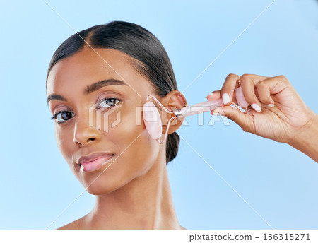 Face, massage and woman with roller, beauty and skincare, natural cosmetics and tools isolated on blue background. Rose quartz, crystal and skin glow, Indian female model in portrait with dermatology Face, massage and woman with roller, beauty and skincare, natural cosmetics and tools isolated on blue background. Rose quartz, crystal and skin glow, Indian female model in portrait with dermatology 136315271