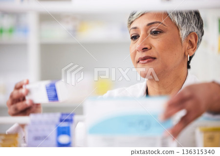 Pharmacist, shelf and a woman with a medicine box in a pharmacy for inventory or prescription. Mature female employee in healthcare, pharmaceutical and medical industry reading product information 136315340