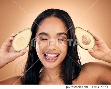 Face, tongue out and woman with avocado for skincare isolated on a brown background in studio. Fruit, funny and happy model with food for nutrition, health or vegan diet, omega 3 or natural cosmetics Face, tongue out and woman with avocado for skincare isolated on a brown background in studio. Fruit, funny and happy model with food for nutrition, health or vegan diet, omega 3 or natural cosmetics 136315341