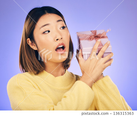 Surprise, gift and box with face of asian woman in studio for birthday, celebration and curious. Thinking, wow and party with female person and present on purple background for giveaway and package Surprise, gift and box with face of asian woman in studio for birthday, celebration and curious. Thinking, wow and party with female person and present on purple background for giveaway and package 136315363