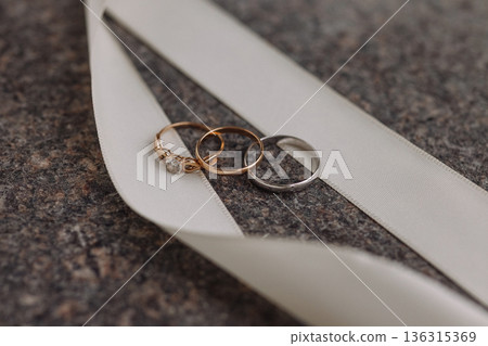 Wedding rings on white ribbon on dark stone surface Wedding rings on white ribbon on dark stone surface 136315369