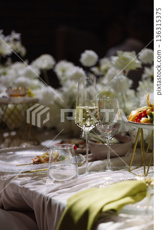 Elegant table setting with champagne glasses, dessert and white flowers on dark background 136315375