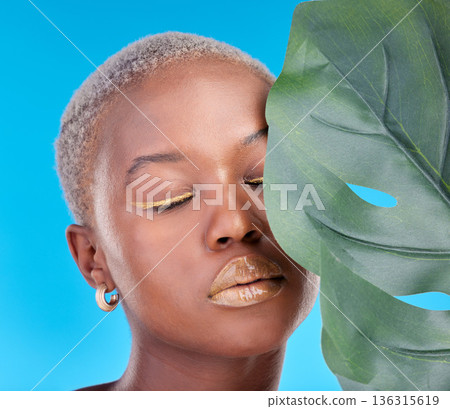 Makeup, plant and a black woman on a blue background for a wellness aesthetic. Face, beauty and an African girl or model with a leaf and organic cosmetics isolated on a studio backdrop for health Makeup, plant and a black woman on a blue background for a wellness aesthetic. Face, beauty and an African girl or model with a leaf and organic cosmetics isolated on a studio backdrop for health 136315619