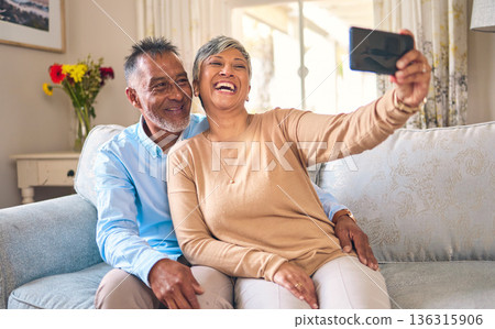 Senior couple, selfie and laughing at home for social media, network connection or memory. Mature man and woman together with smartphone for a profile picture with a smile and love on a lounge sofa Senior couple, selfie and laughing at home for social media, network connection or memory. Mature man and woman together with smartphone for a profile picture with a smile and love on a lounge sofa 136315906