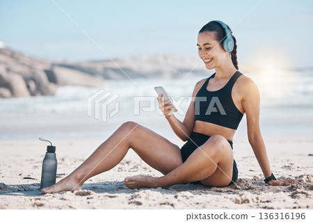 Fitness, break and happy woman relax at beach with phone, music and headphones after training. Exercise, resting and lady health influencer posting to social media, blog or podcast after ocean run Fitness, break and happy woman relax at beach with phone, music and headphones after training. Exercise, resting and lady health influencer posting to social media, blog or podcast after ocean run 136316196