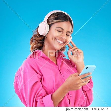 Happy, woman and smartphone, headphones and music with audio streaming isolated on blue background. Entertainment, happiness and fun with female person listening to podcast or radio on mobile app Happy, woman and smartphone, headphones and music with audio streaming isolated on blue background. Entertainment, happiness and fun with female person listening to podcast or radio on mobile app 136316484