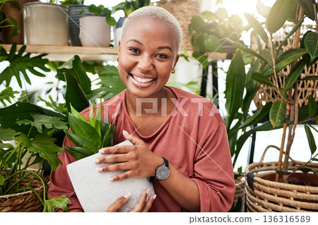 Happy, eco friendly and portrait of a woman with a plant in the nursery for a sustainable gift. Happiness, smile and African female person with green leaves in pot in greenhouse for gardening at home Happy, eco friendly and portrait of a woman with a plant in the nursery for a sustainable gift. Happiness, smile and African female person with green leaves in pot in greenhouse for gardening at home 136316589