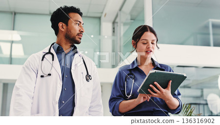 Doctors, talk and tablet in lobby with team, review and check schedule for healthcare services at clinic. People, medical staff and tech with application, low angle and walk in hallway at hospital 136316902