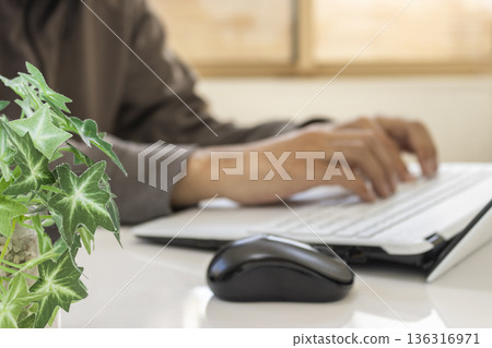 一張照片顯示，一名男子在明亮的房間裡靠窗遠端辦公（焦點在前景的植物上，沒有拍到人臉）。 136316971