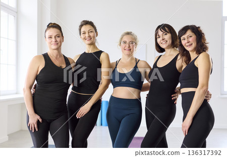 Friendly yoga group of women smiling together after training in a bright studio Friendly yoga group of women smiling together after training in a bright studio 136317392