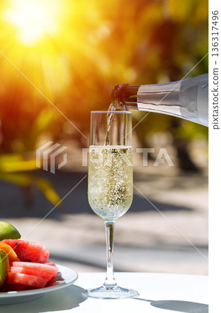 Pouring a champagne into flute glass, amazing fizz and bubbles in sparkling wine, table served with fruit plate at outdoor restaurant on sunset with sun beams Pouring a champagne into flute glass, amazing fizz and bubbles in sparkling wine, table served with fruit plate at outdoor restaurant on sunset with sun beams 136317496