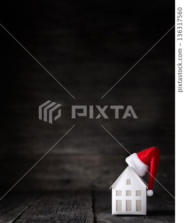 Santa Claus hat on model of house, closeup. Isolated on wooden background. Christmas celebration. Winter holidays Santa Claus hat on model of house, closeup. Isolated on wooden background. Christmas celebration. Winter holidays 136317560