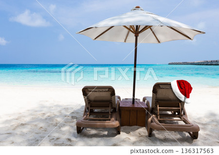 Santa Claus hat on tan chairs under white parasol on turquoise sea beach, perfect vacation on Maldives island. Christmas and New Year celebration 136317563