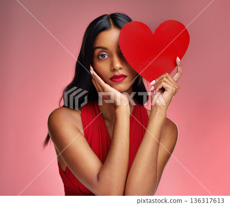 Woman, paper heart and face in studio portrait for makeup, beauty or romantic sign by red background. Girl, fashion model and cardboard emoji with love for cosmetic, valentines day date and aesthetic 136317613