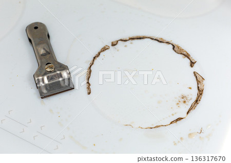 Special steel scraper on dirty white ceramic kitchen stove after cooking. Concept of homecleaning Special steel scraper on dirty white ceramic kitchen stove after cooking. Concept of homecleaning 136317670