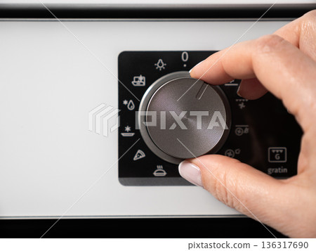 Woman adjusting modern white oven in kitchen.  Female hand pushing and turning knobs on oven control panel 136317690