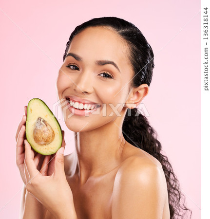 Beauty, avocado and face of a happy woman with skin care, dermatology and natural glow. Portrait of female aesthetic model with fruit for moisturizer, cosmetics or diet nutrition on a pink background Beauty, avocado and face of a happy woman with skin care, dermatology and natural glow. Portrait of female aesthetic model with fruit for moisturizer, cosmetics or diet nutrition on a pink background 136318144