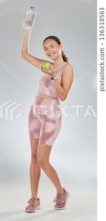 Portrait, happy woman and fitness with apple, water and studio to celebrate diet, healthy goals or detox wellness. Excited female sports model, liquid bottle or fruit of nutrition on white background 136318563