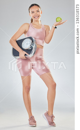 Apple, scale and fitness portrait of woman on diet in studio for healthy results, weightloss goals and progress. Exercise, body nutrition and female model lose weight with fruit on white background Apple, scale and fitness portrait of woman on diet in studio for healthy results, weightloss goals and progress. Exercise, body nutrition and female model lose weight with fruit on white background 136318573