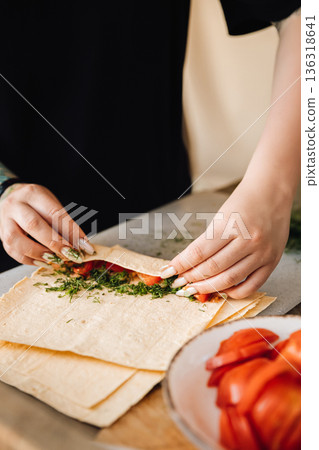 Hands rolling lavash wrap with tomatoes and herbs on kitchen table Hands rolling lavash wrap with tomatoes and herbs on kitchen table 136318641