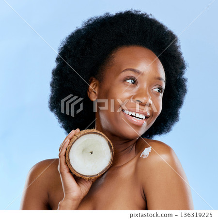 Beauty, skin and coconut with a model black woman in studio on a blue background for natural treatment. Thinking, skincare and cosmetics with a happy young female person holding fruit for oil 136319225