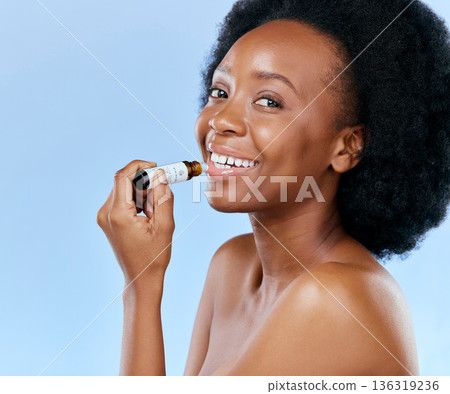 Portrait, skincare and lip balm with a black woman in studio on a blue background for natural cosmetics. Face, hydration and moisture with a happy young female model holding a beauty product for care 136319236