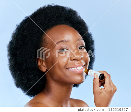 Portrait, beauty and lip balm with a black woman in studio on a blue background for skincare cosmetics. Face, hydration and moisture with a happy young female model holding a makeup product for care 136319237