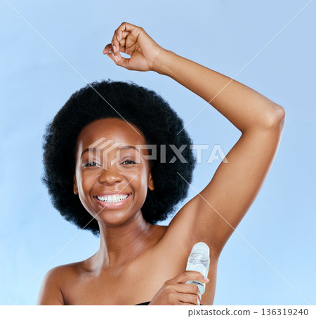 Face, deodorant and armpit of black woman in studio isolated on a blue background. Portrait, underarm and happy model with roll on product for cosmetics, cleaning and hygiene, wellness or fresh scent 136319240