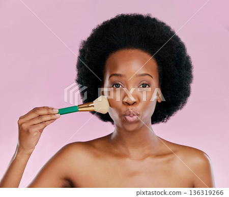 Face, makeup and black woman with brush, kiss and beauty in studio isolated on a pink background. Portrait, facial cosmetics and African model apply foundation, powder and wellness for skincare pout. 136319266
